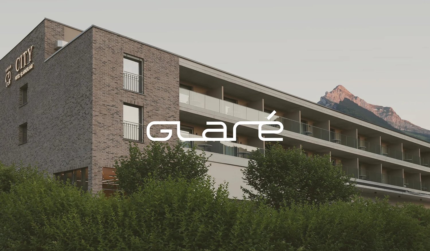 The wordmark in white over the hotel building, with mountains behind