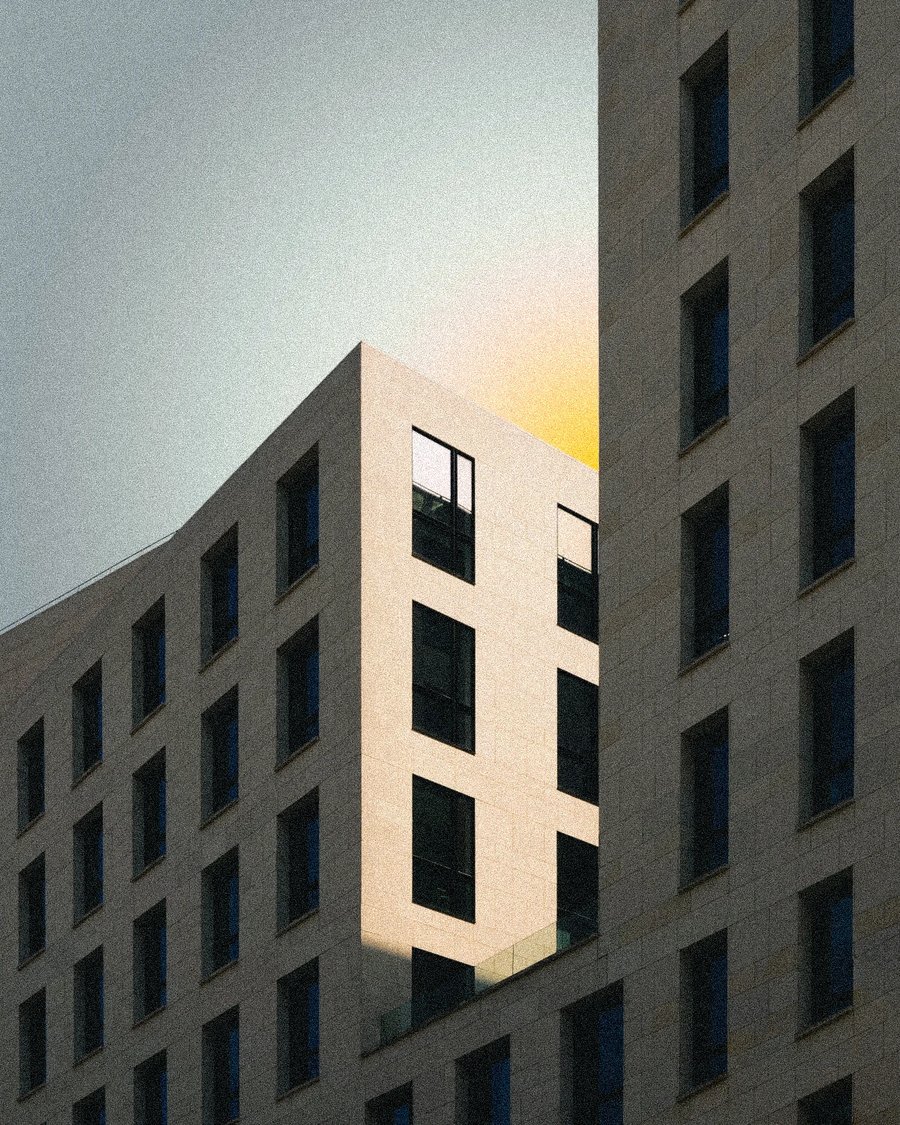 Prenaj Immobilien — pale stone apartment buildings with rows of deep windows, a yellow glow in the sky behind them